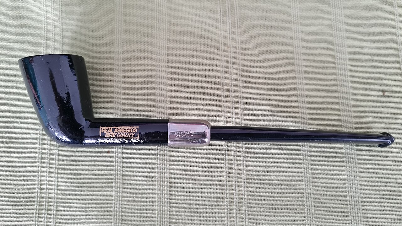 A mostly black, shiny smoking pipe. The pipe has text on it in capital letters that reads, “REAL ASBESTOS. BEST QUALITY”